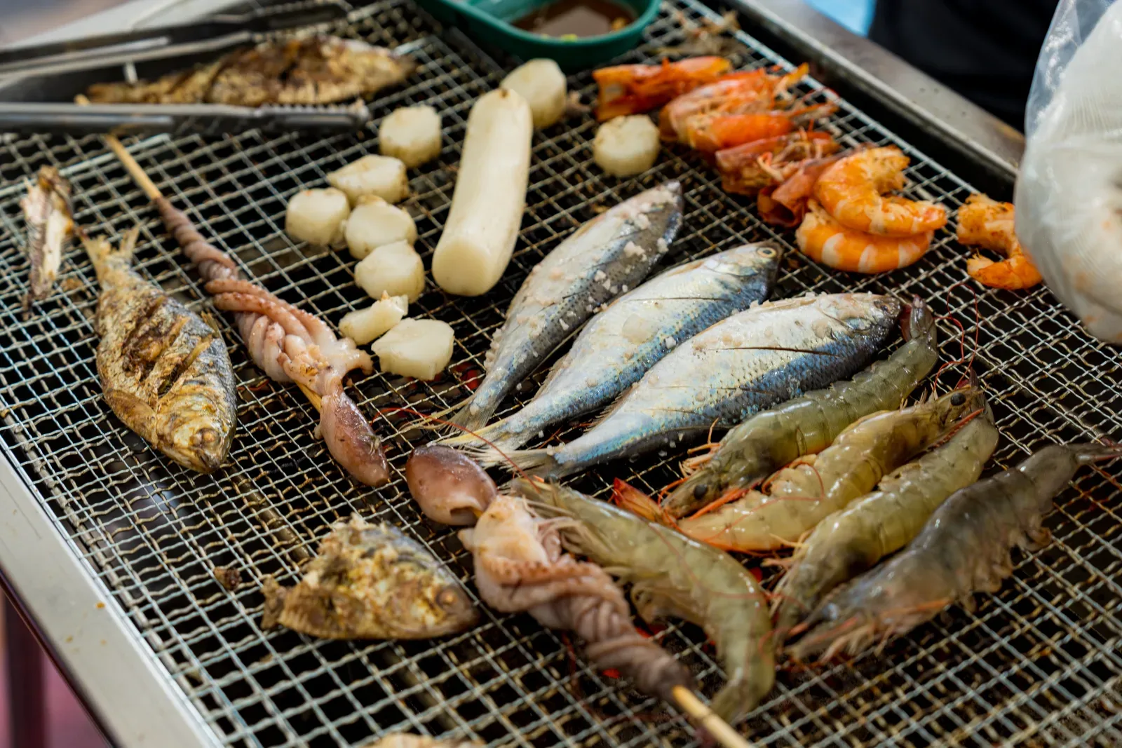 그릴 위에서 굵은 대하, 전어 등 해산물이 맛있게 구워지고 있는 장면.