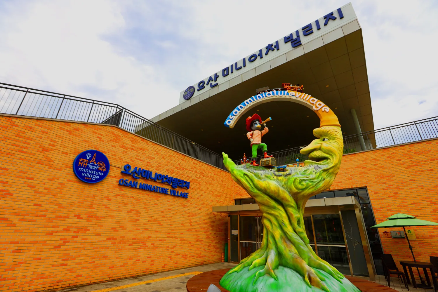 오산미니어처빌리지 건물 정면과 앞에 설치된 큰 캐릭터 조형물의 전경 이미지.
