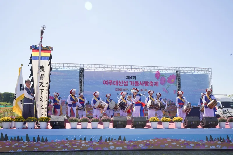 전통 복장을 입고 북과 장구를 연주하는 공연단이 무대 위에서 공연하는 모습.