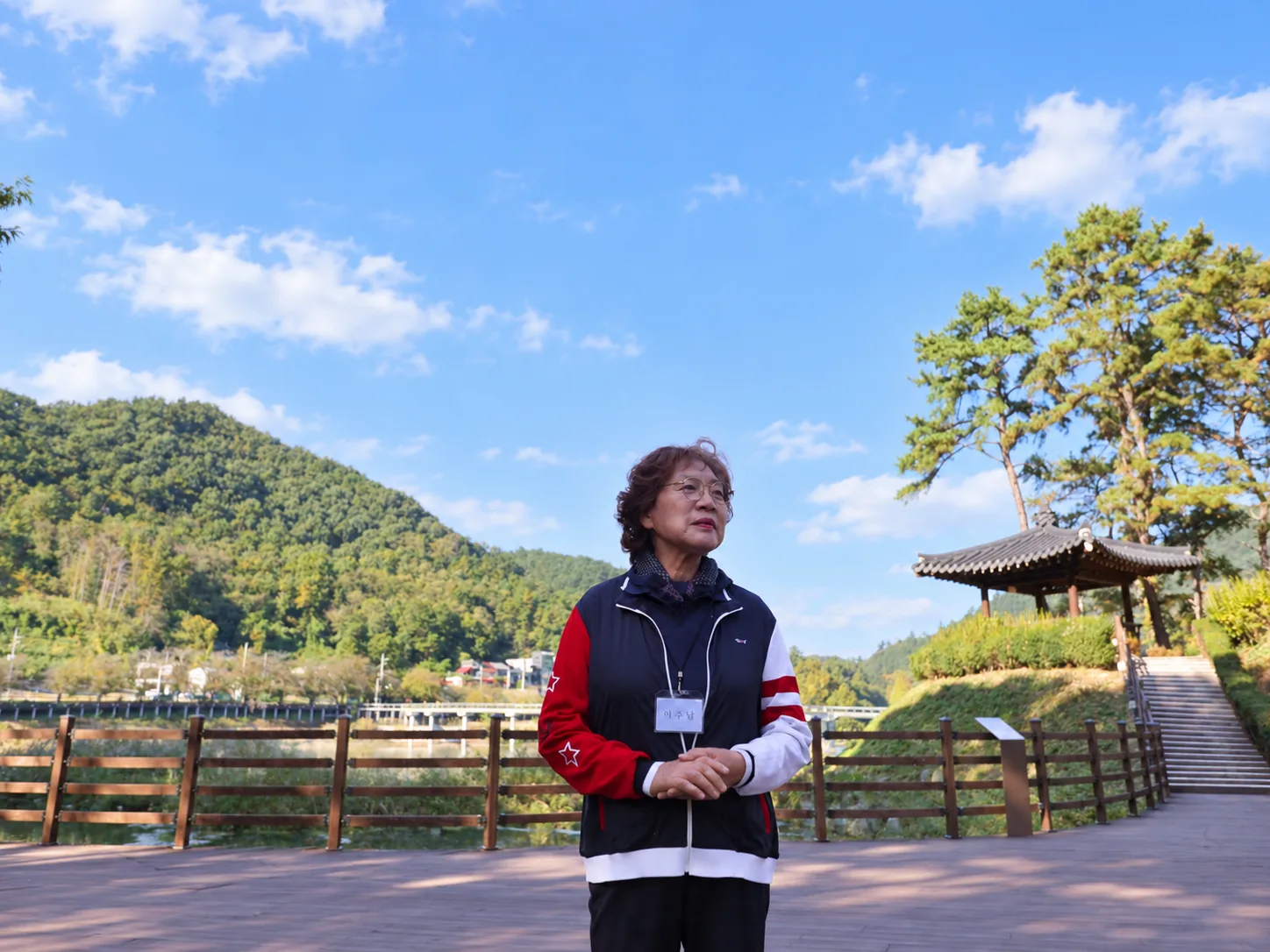 푸른 산과 전통 누각을 배경으로 인터뷰 중인 중년 여성 회원 모습.