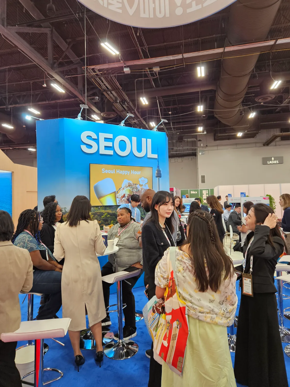 서울 해피아워 부스에서 모여 앉아 대화하며 한국 치킨과 맥주를 즐기는 다수의 사람들 모습
