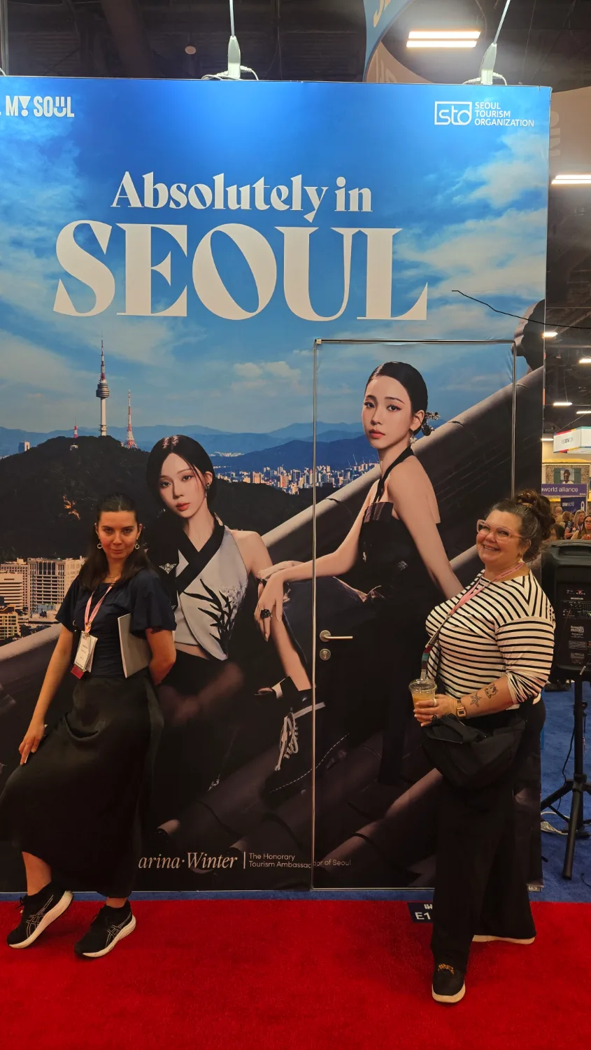 서울 홍보 부스에 설치된 에스파 대형 화보 앞에 서서 기념촬영하는 두 명의 참가자 모습