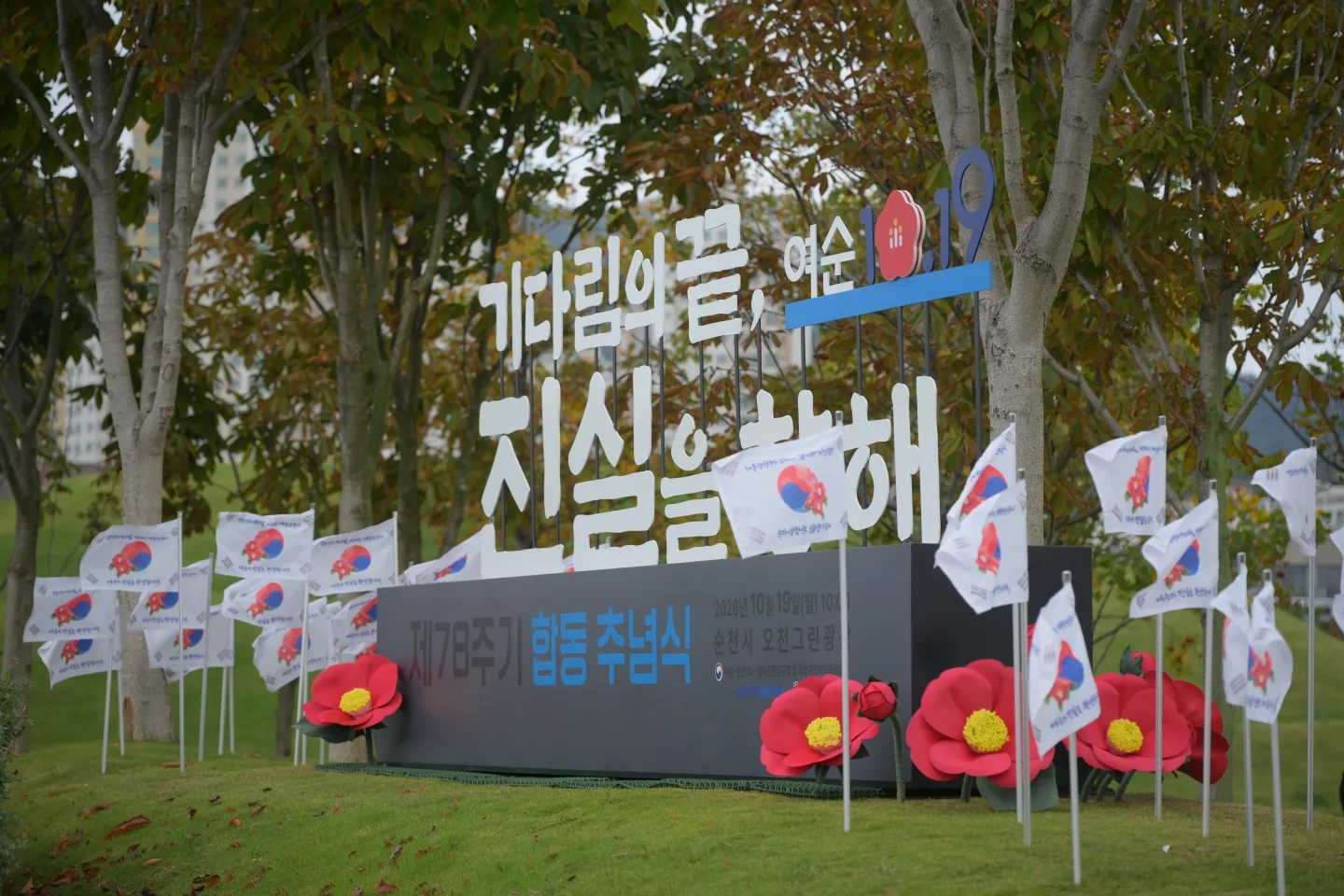 나무들이 있는 야외 공간에 '기다림의 끝 여순 진실을 완성' 문구와 태극기 깃발 여러 개가 세워져 있는 추념식 행사장 모습.