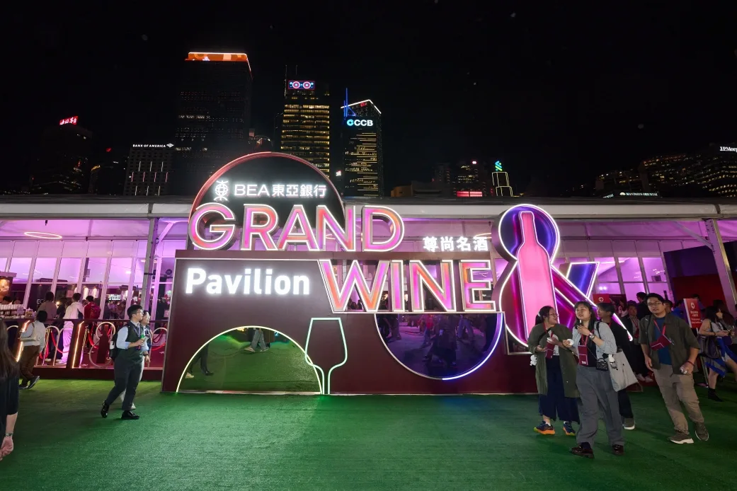 밤에 'GRAND WINE Pavilion' 네온 조명 아래 축제 방문객들이 모여있는 장면으로 빅토리아 하버 야경이 배경에 보임.