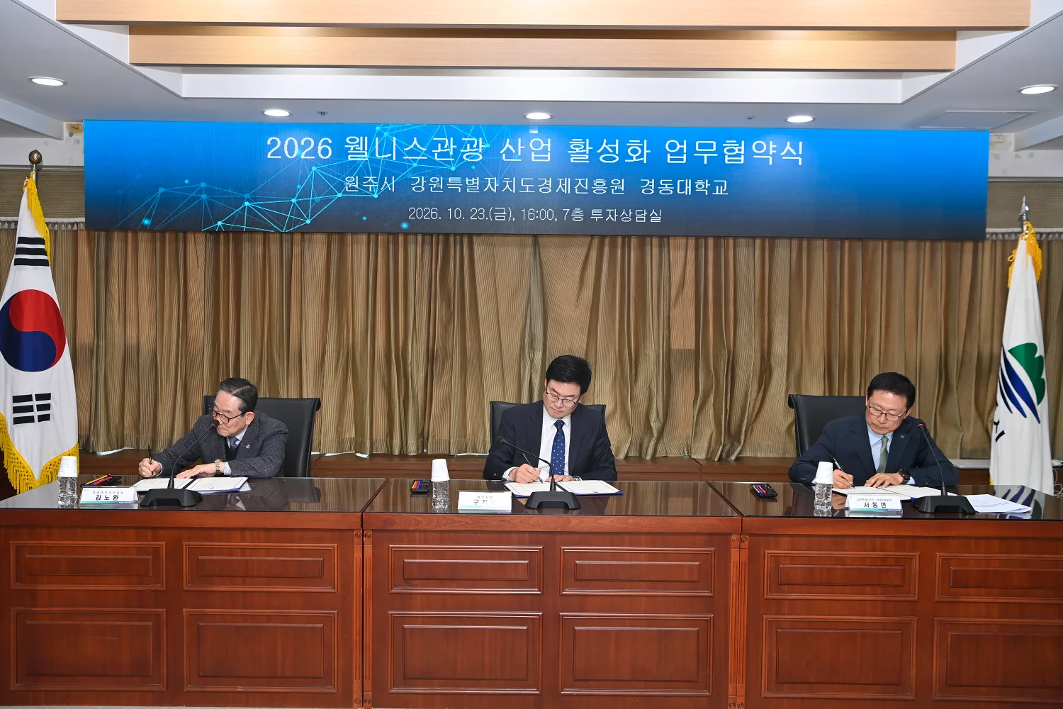 회의 테이블 앞에 앉아 서류에 사인하는 세 명의 관계자 모습