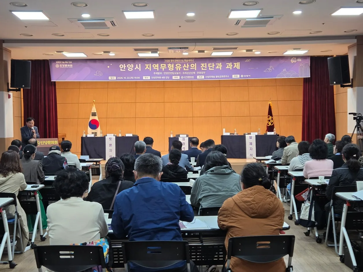 회의실 앞쪽 무대와 스크린, 뒤쪽에 앉은 많은 참석자들의 뒷모습 장면