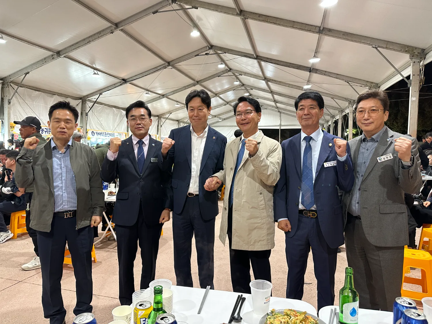 실내 행사 공간에서 양복과 캐주얼 복장을 한 남성 여섯 명이 나란히 서서 주먹을 쥐고 다짐하는 모습