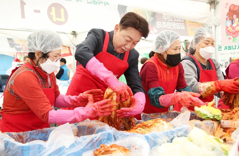 사회자가 행사에 참여한 여러 사람이 함께 배추에 양념을 버무리며 김장을 하는 모습