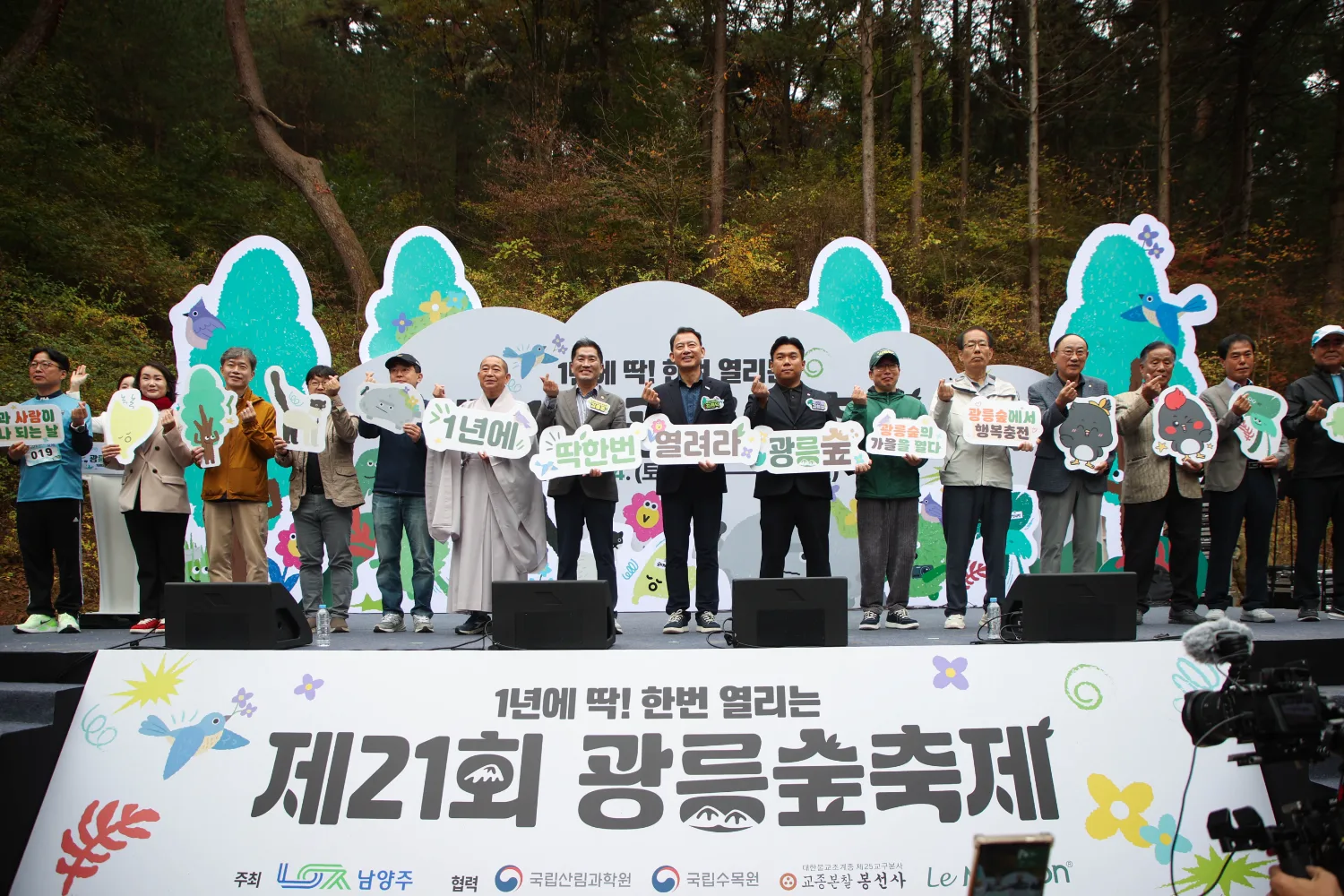 무대 위에 시민들과 내빈들이 여러 명 나란히 서서 다양한 메시지와 그림이 담긴 피켓을 들고 있는 모습.