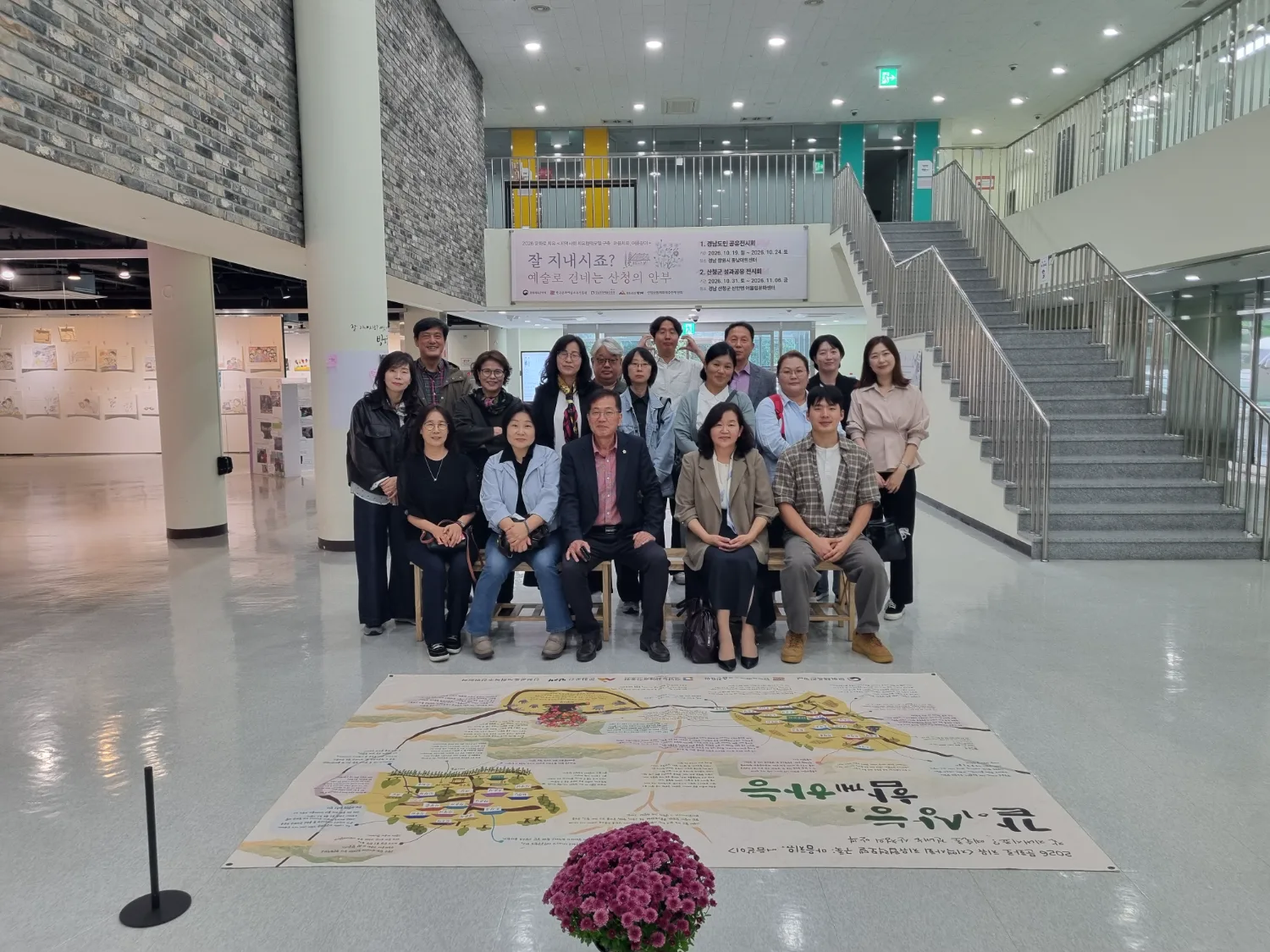 실내 전시 공간에서 주민 및 관계자 15명이 모여 앉거나 서서 카메라를 바라보고 있는 단체 사진