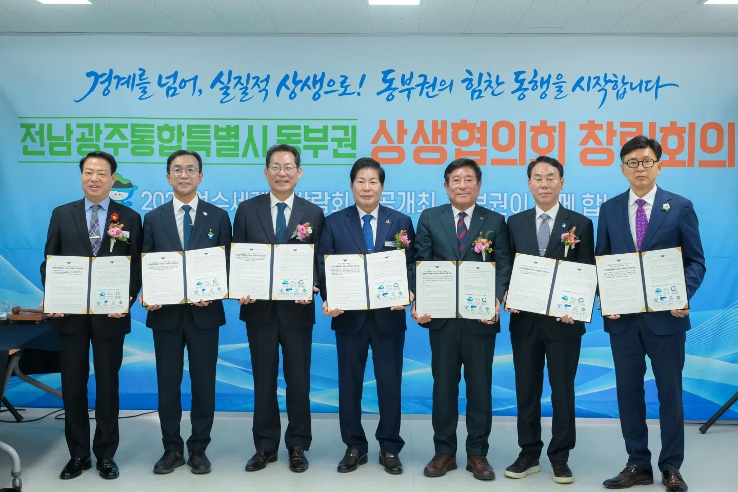 정장 차림의 7명의 시·군 단체장이 서서 손에 서류를 들고 기념 촬영하는 모습