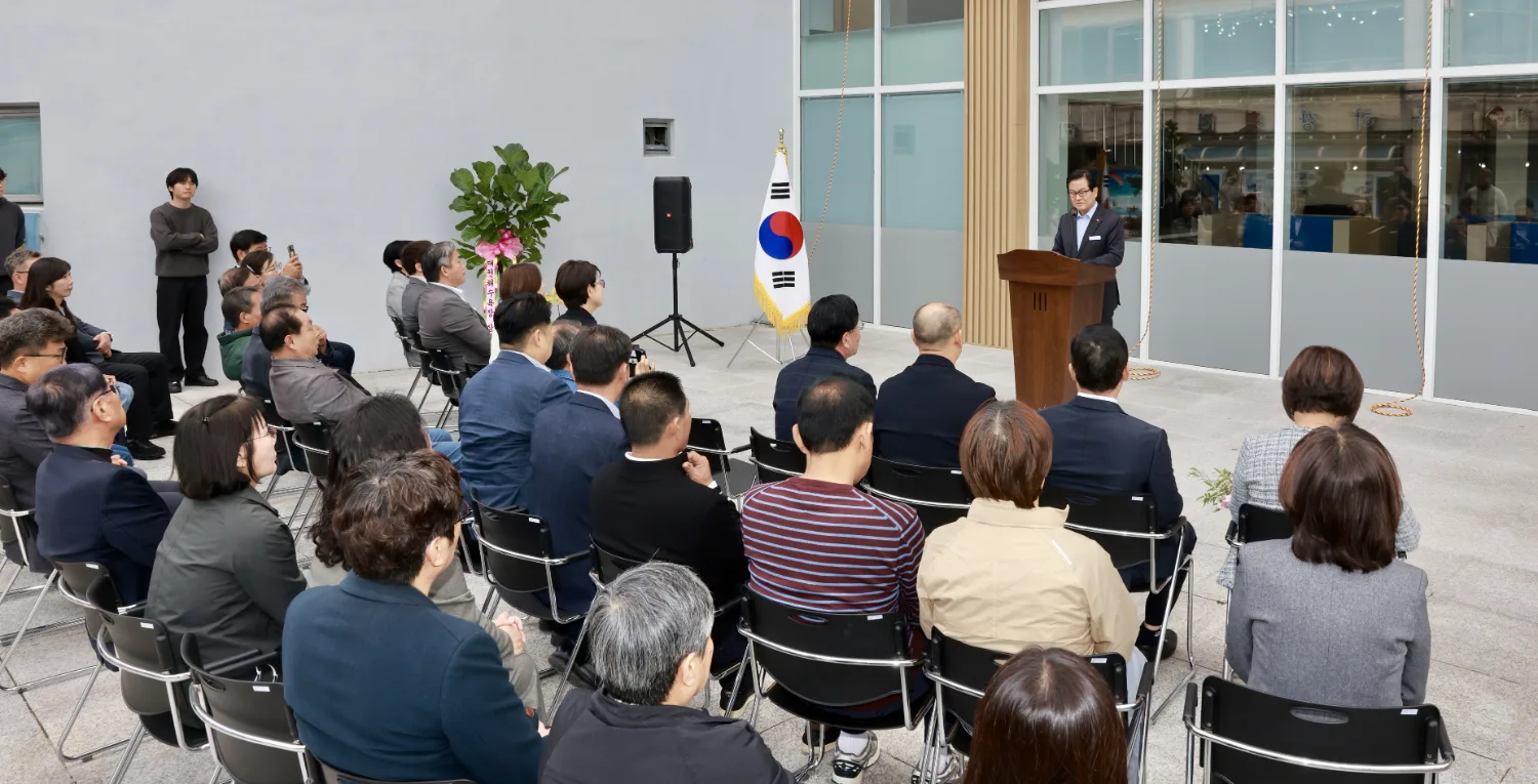 보령워케이션 센터 입구 앞에서 한 남성이 마이크를 잡고 연설하고 있으며, 여러 참석자들이 의자에 앉아 주의 깊게 듣고 있다.