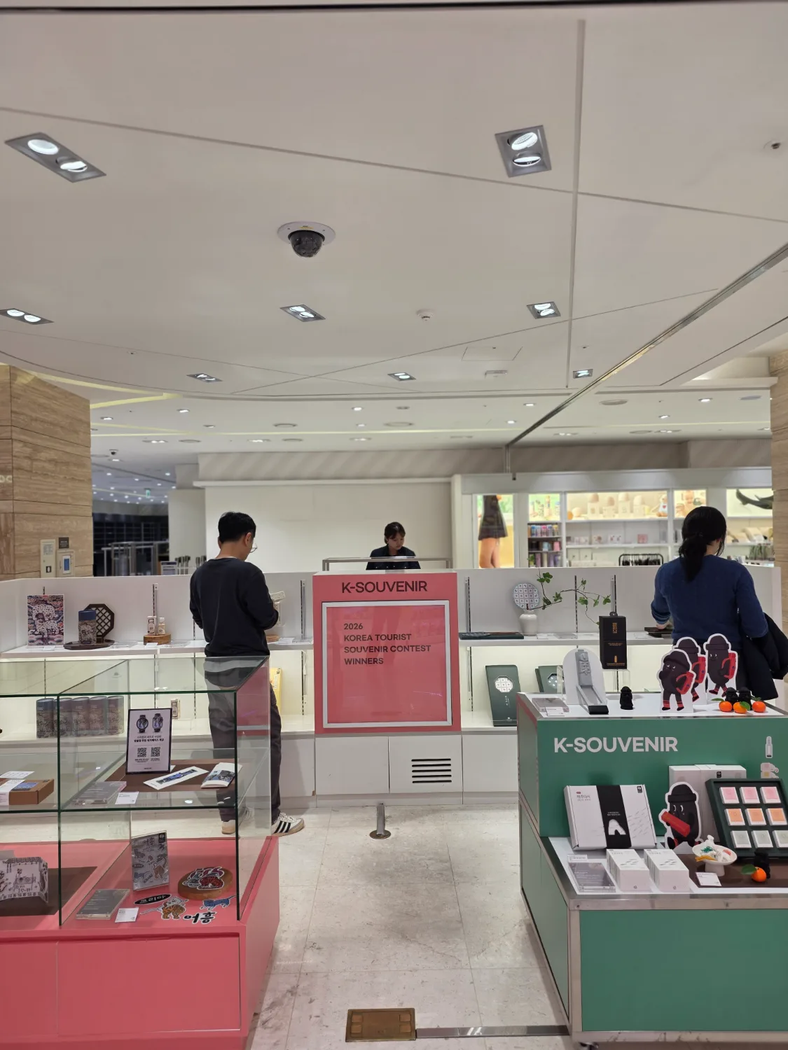 롯데면세점 제주점 매장 내 한국 관광기념품이 진열된 유리 케이스와 선반 위에 제품들이 놓여 있고, 방문객들이 상품을 둘러보고 있다.